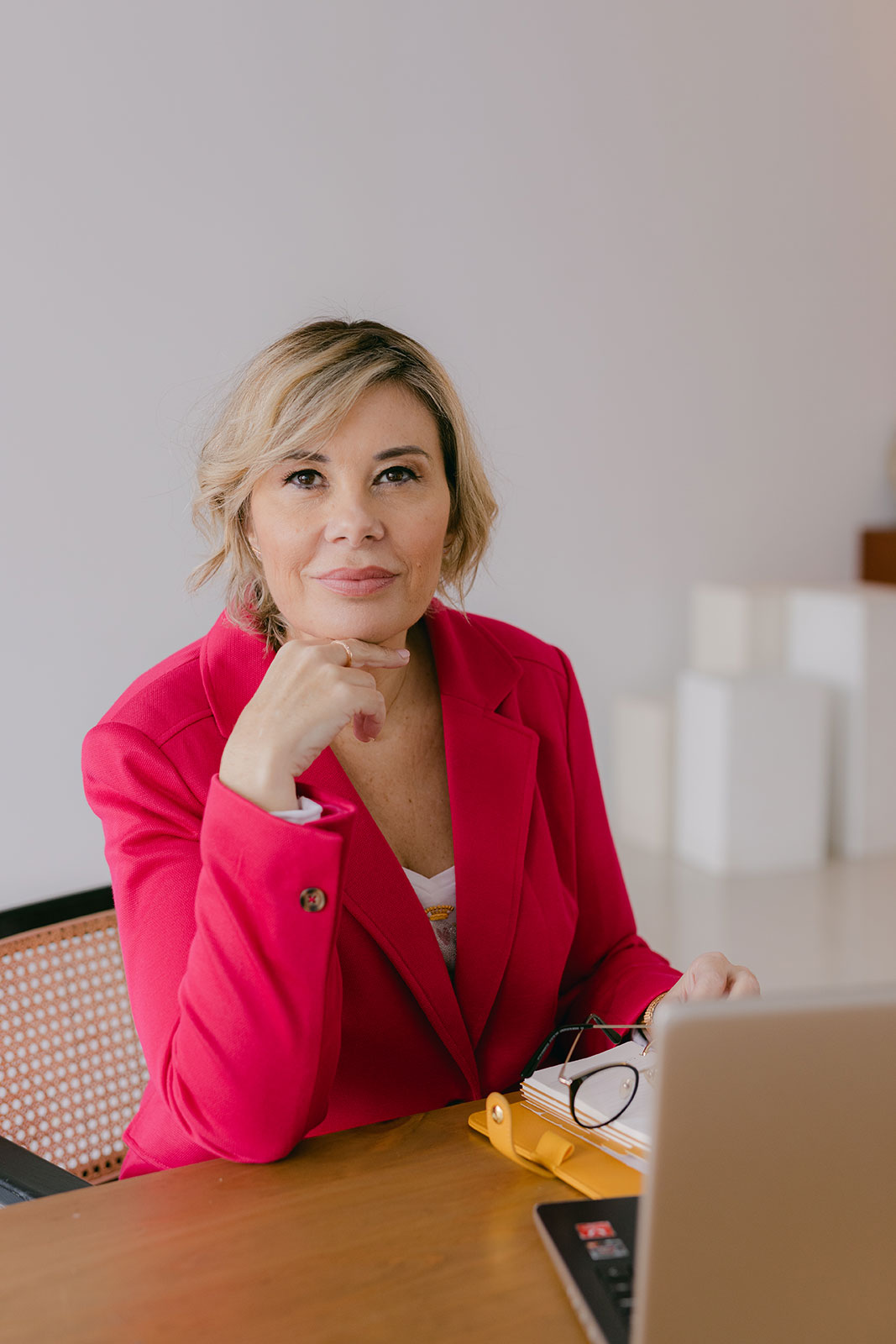 portrait of business enterpreneur woman wearing pink suit and sitiing in her office with laptop and glasses on the table