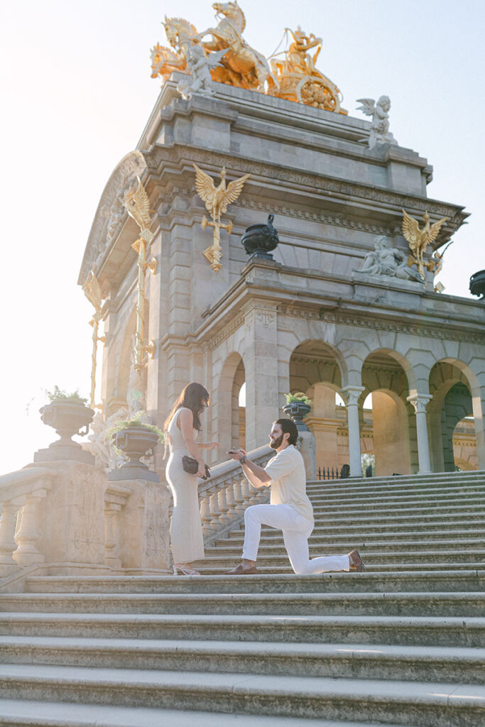 Man wearing white outfit proposing to his girlfiend in Ciutadella Park with gorgeous view in Barcelona