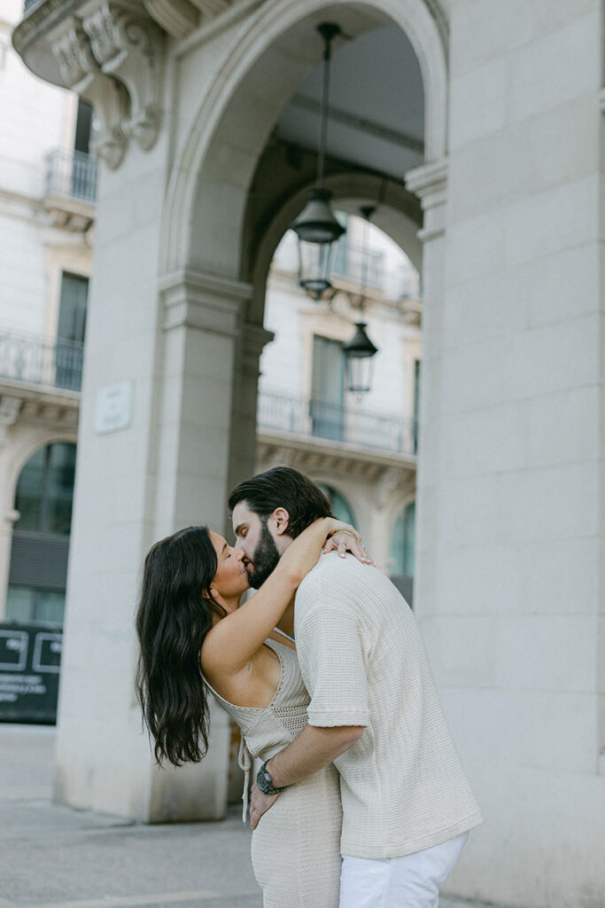 Portrait of young stylish couple kissing in front of beautiful architecture of El Borne after the surprise proposal in Barcelona