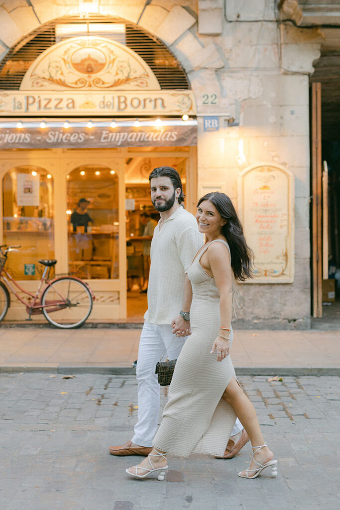 Happy couple wearing smart casual outfits in beig tones are walking down the streets of El Borne after the serprise proposal in Barcelona