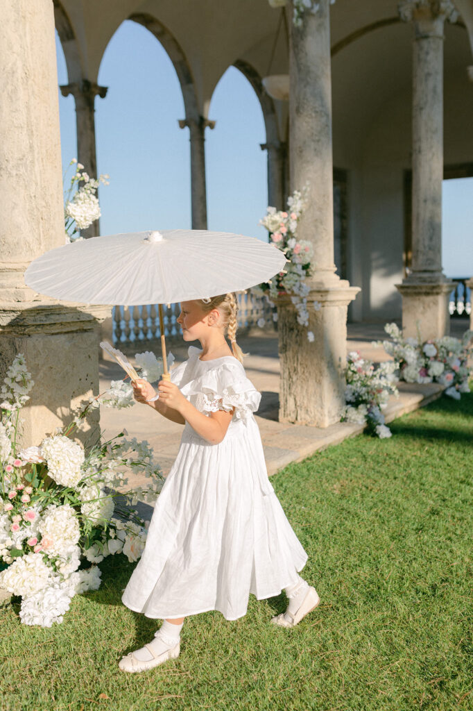 Little girl wearing white dress and umbrella at mediterranean wedding at luxury hotel in Spain - Lena Karelova Photography
