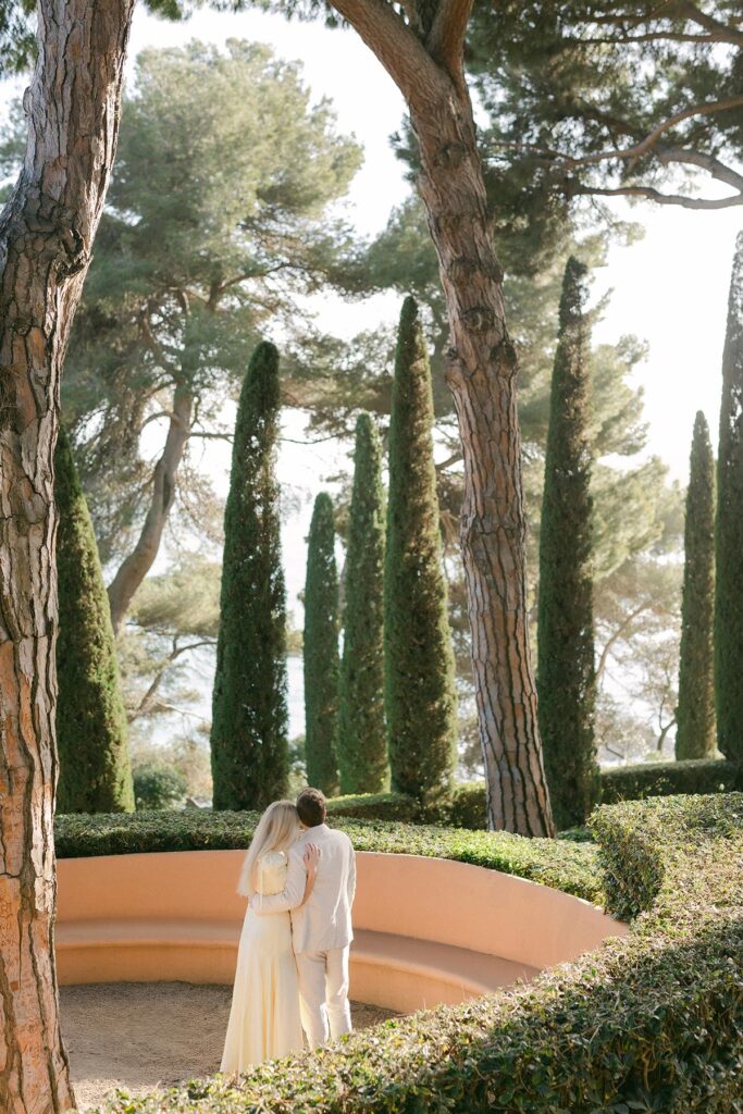 Romantic moment of couple hugging under pine trees with ocean views at their Costa Brava engagement shoot.Captured by an experienced Barcelona engagement photographer
