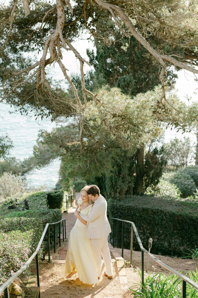 Romantic moment of couple hugging under pine trees with ocean views at their Costa Brava engagement shoot. Captured by an experienced Barcelona engagement photographer