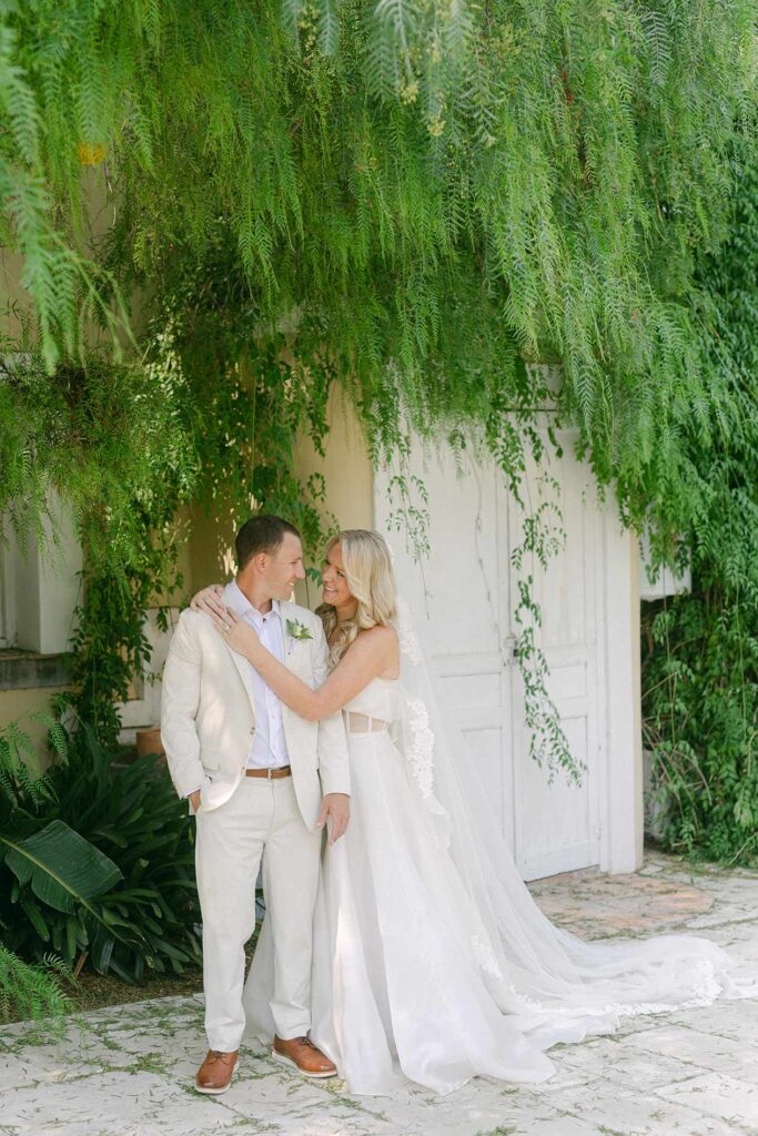 Bride and groom embracing beneath lush greenery during a villa wedding in Barcelona.