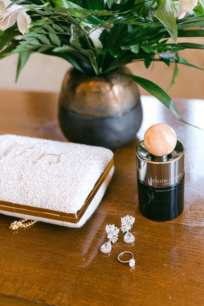 Bridal details with earrings, engagement ring, perfume, and beaded clutch at Hostal La Gavina