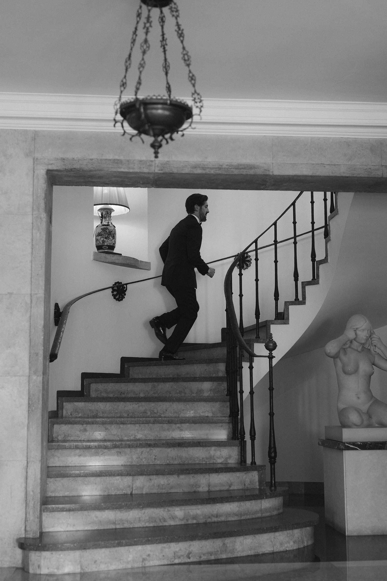 Black and white photo of groom Gonzalo walking up the staircase at Hostal La Gavina