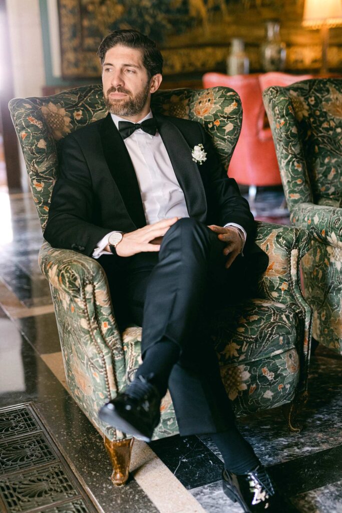Portrait of the groom seated in an armchair during his wedding portrait session at Hostal La Gavina