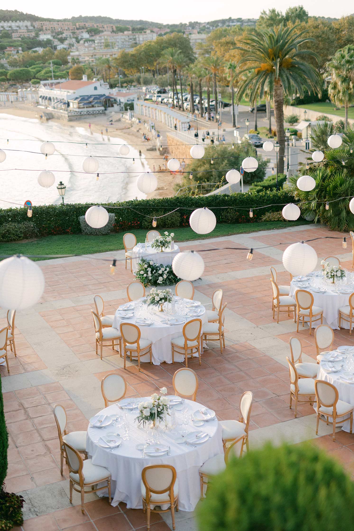 Elevated view of an outdoor wedding reception on a terrace overlooking the Costa Brava coast.